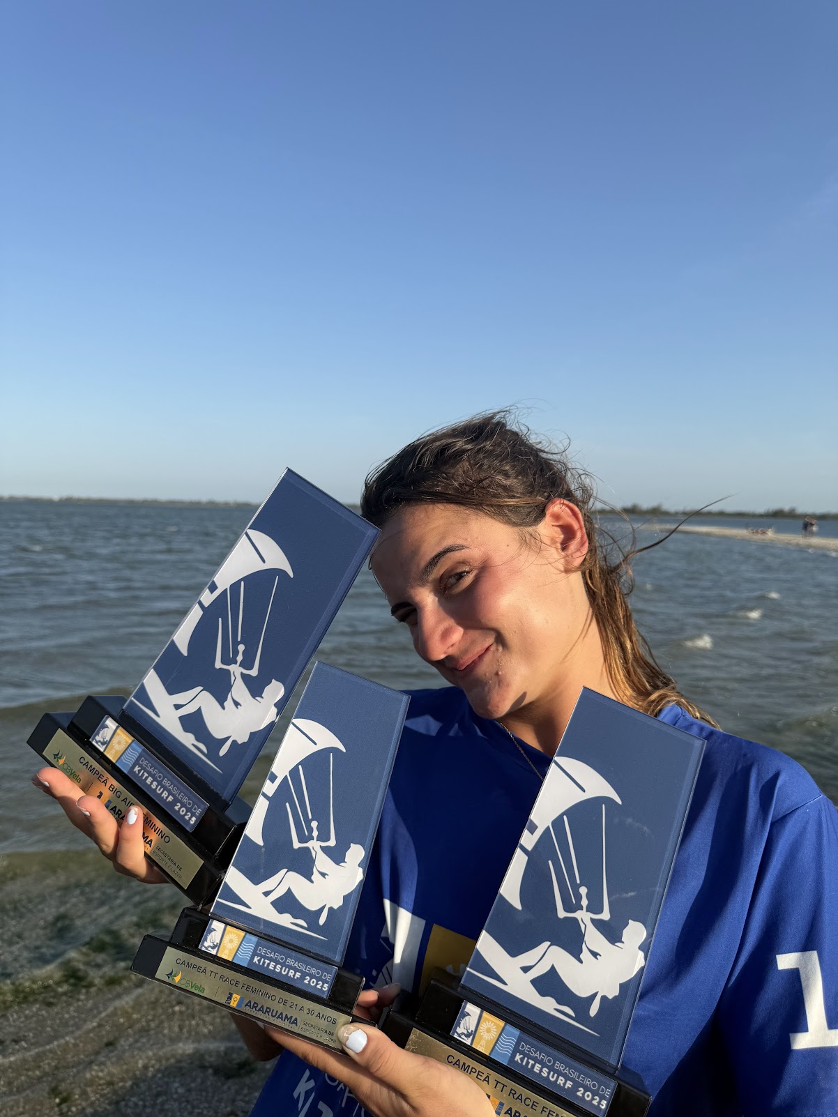 Gabi segurando três troféus depois de vencer no kitesurf