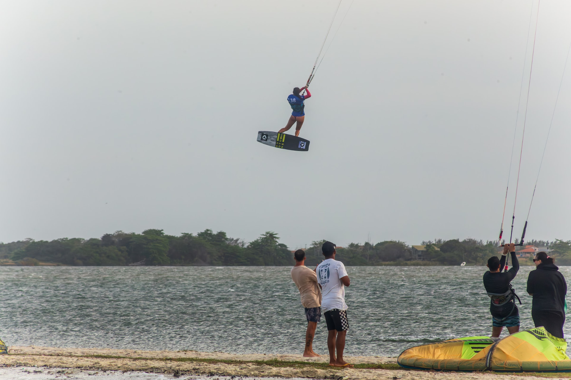 Gabi saltando alto em campeonato de kitesurf com atletas na praia